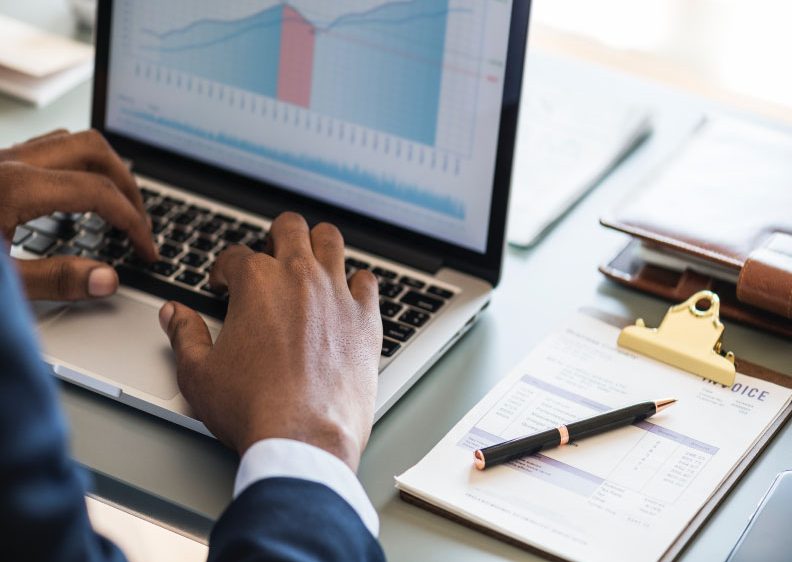 Pair of hands using a laptop next to an invoice on a clipboard