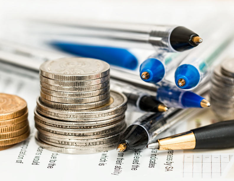 Closeup of a few small stacks of coins next to several ballpoint pens